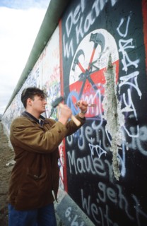 A West German man uses a hammer and chisel to chip off a piece of the Berlin Wall as a souvenir.  A portion of the Wall has already been demolished at Potsdamer Platz..