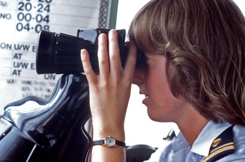 1980s Coast Guard - A female lieutenent junior grade officer piers through a pair of binoculars while on operations duty.