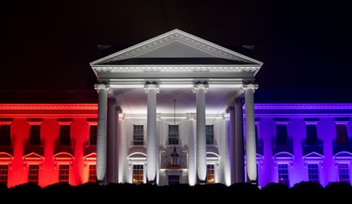 The White House North Portico is lit in red-white and blue lights