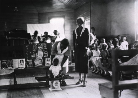 Preschool child is weighed by African American nurse