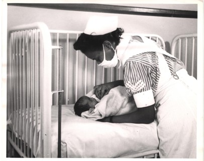 A nurse is leaning over a newborn in a crib.
