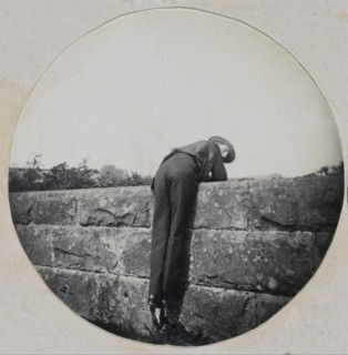 Man in Hat Bent Over a Stone Wall