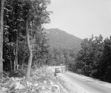 Men standing outside a car on a rural road ca.  between 1910 and 1926