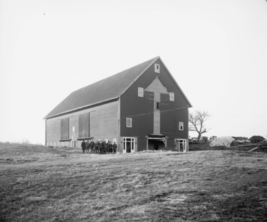Men and women standing outside a barn  ca.  between 1910 and 1926
