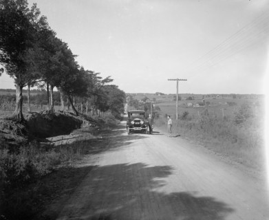 Two men standing outside a car on a rural road ca.  between 1910 and 1926