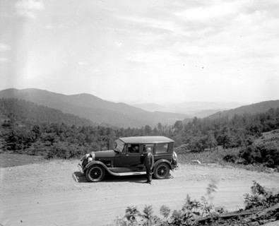 Man standing outside his automobile on a rural mountain road  ca.  between 1910 and 1926