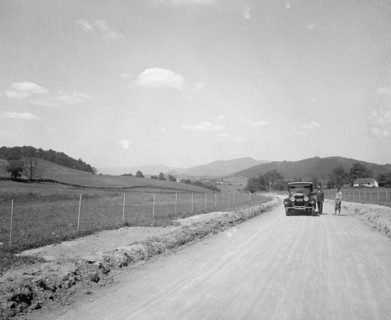 Two men standing outside an automobile on a rural road ca.  between 1910 and 1926