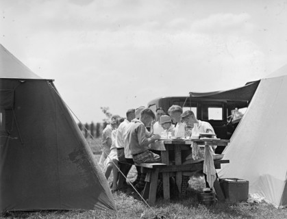 A family eating at a picnic table while camping in the early 20th century ca. between 1909 and 1923