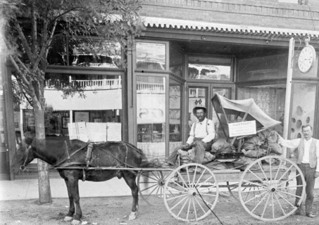 Man sitting in a horse drawn wagon in front of a store ca. between 1909 and 1923