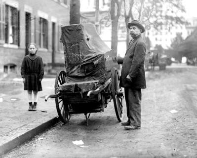 Child standing next to an organ grinder with his organ ca. between 1909 and 1940