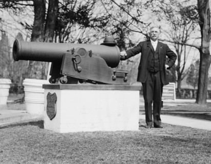 J.F. Schnell, Superintendent of  Battle Cemetery standing next to a cannon ca. between 1909 and 1919