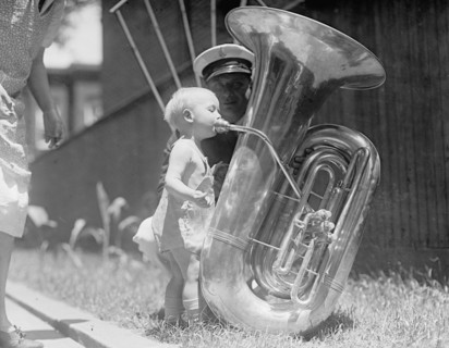 A toddler blowing on a tuba or euphonium ca. between 1909 and 1923