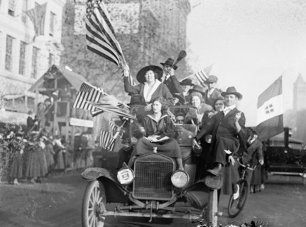Men and women in an overcrowded car waving American flags during a peace demonstration ca.  1918