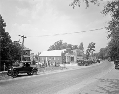 Early 1900s street scene, car driving down a road in small town ca.  between 1918 and 1928