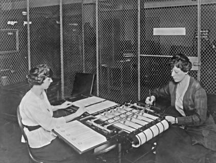 Two women using check signing machine which signs checks issued by the War Risk Bureau, Washington, D.C. ca. between 1909 and 1932