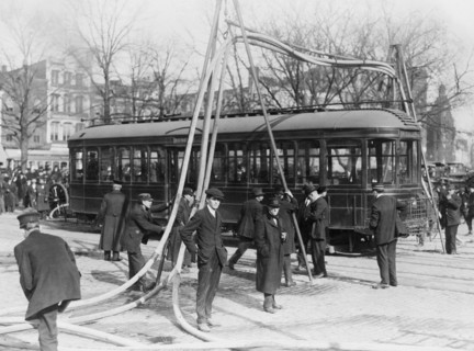 Firemen with hoses stretched over a streetcar ca. 1909