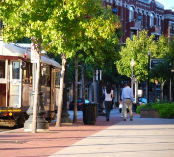 A man and woman walking north on McKinney Avenue in the Uptown area of Dallas, TX; a trolley car stopped on the street