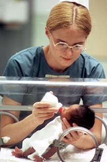 A nurse feeds an infant in an incubator.