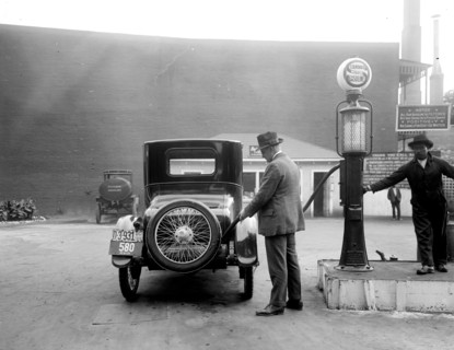 Man pumping gas into his automobile in early 1900s