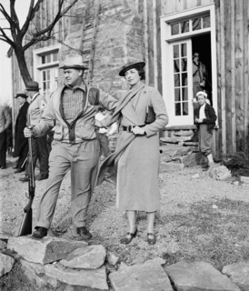Well dressed woman with man holding rifle or shotgun