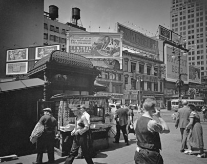 Men and women hurry past newstand outside uptown subway entrance, street beyond is lined with businesses topped with large billboards. Union Square, 14th Street and Broadway, Manhattan. ca. 1936