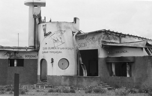 1947 - Ruin of a burnt-out building with graffiti. Boot with nazi cross (swastika) on back of woman with child. Text: Djika Blanda and Djangan Mendjadjah, among others. -  Location: Indonesia, Java, D...