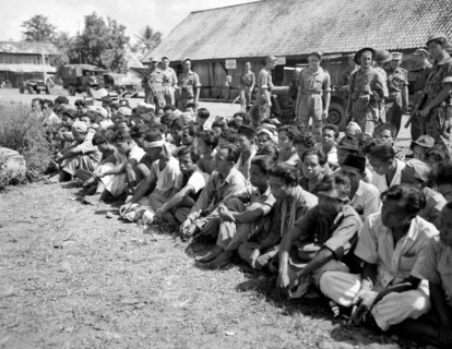 Indonesia History - Indonesian prisoners of war or detainees sit in lotus seat on the ground guarded by Dutch soldiers