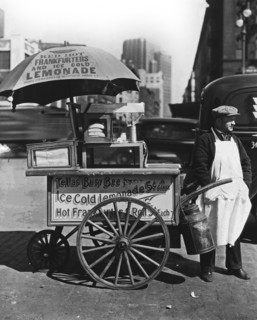 1930s New York City - Hot Dog Stand, West St. and North Moore. Vendor stands next to his Tellas Busy Bee cart, advertising 'Red Hot Frankfurters and Ice Cold Lemonade' ca. 1936