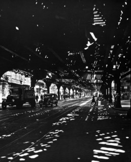1930s New York City - Patterns of light illuminate darkness under elevated railroad tracks, pedestrians, car, truck visible ca. 1936