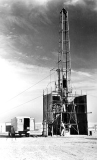 Dr. Robert Goddard's 22 foot rocket in it's launching tower, 1940, near Roswell, New Mexico. N.T. Ljungquist on the ground, A.W. Kisk working on rocket and C. Mansur at top of tower.