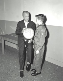 Mercury astronaut John Glenn holding a globe while talking with young boy, a boy scout or cub scout.