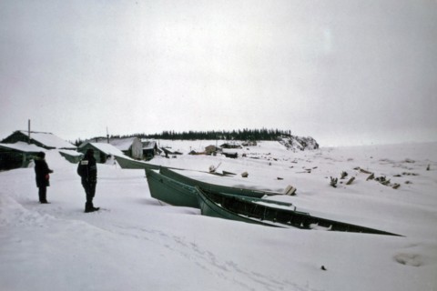 Men looking out at boats on the Elim Alaska coastline ca. March 1974