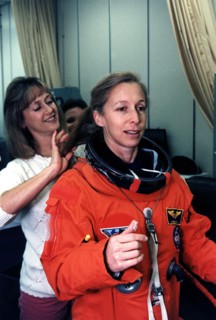 STS-81 Mission Specialist Marsha S. Ivins gets a helping hand from a suit technician as she prepares to don the helmet of her launch/entry suit in the suitup room of the Operations and Checkout (O&C) ...