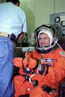 STS-94 Mission Commander James D. Halsell, Jr., puts his left glove on while he is assisted into his launch/entry suit in the Operations and Checkout (O&C) Building