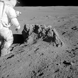 Astronaut Alan Shepard stands beside large boulder found by Apollo 14 crew
