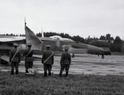Four officers with regimental banner stand against the MiG-23 taxiing out for takeoff, air base Kubinka, USSR.