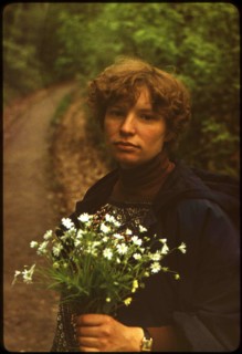Young caucasian woman with a bouquet of daisies on a background of the road, turning to the forest.