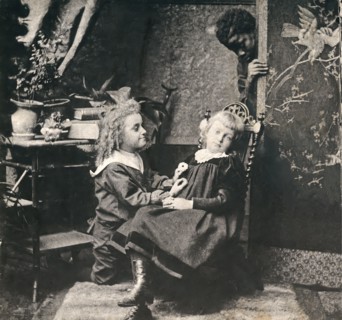 A boy and a girl with a black man looking on from behind a screen.