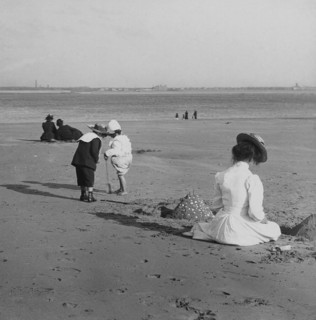 Beach scene with children playing and adults sitting in the sun.