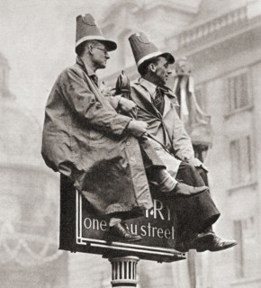 Two men atop a traffic sign in order to get a better view of the Coronation procession of George VI and Queen Elizabeth.