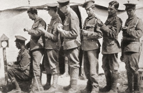 Soldiers during World War One sychronising their watches with a clock mounted on a post in the camp.