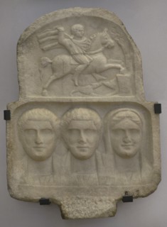 Family group: busts of two bearded men and a woman. Above: relief depicting Heros, the Thracian