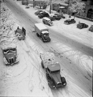 Snowfall in Lausanne: Trucks driving on a snowy street; 1952.