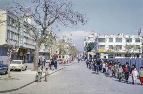 Primary school children walking hand in hand along city centre commercial street, Macau, Asia 1964.