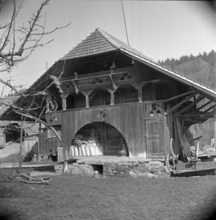 Man bundling firewood in front of a granary in Wynigen BE 1960
