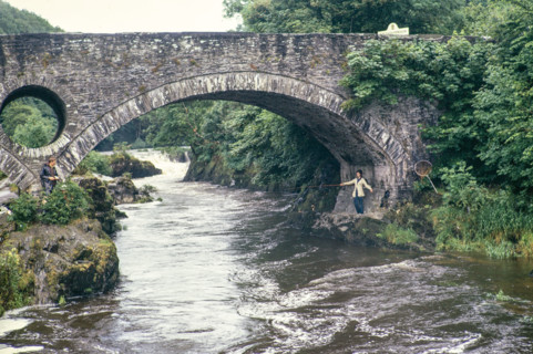 Woman fishing standing under bridge.