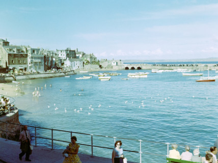 Boats at moorings in the harbour people swimming in sea from beach at St Ives.