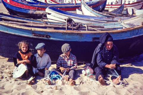 Fisherman and children repairing nets on beach by traditional fishing boats.