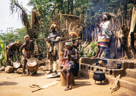 group of Zulu people dressed in traditional attire, performing an outdoor ceremony at a village, likely in the KwaZulu-Natal province of South Africa.