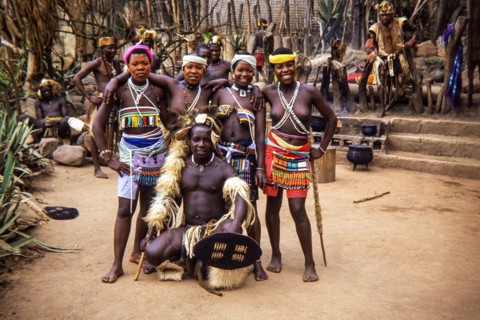 A group of Zulu people in traditional attire at a cultural village in South Africa.